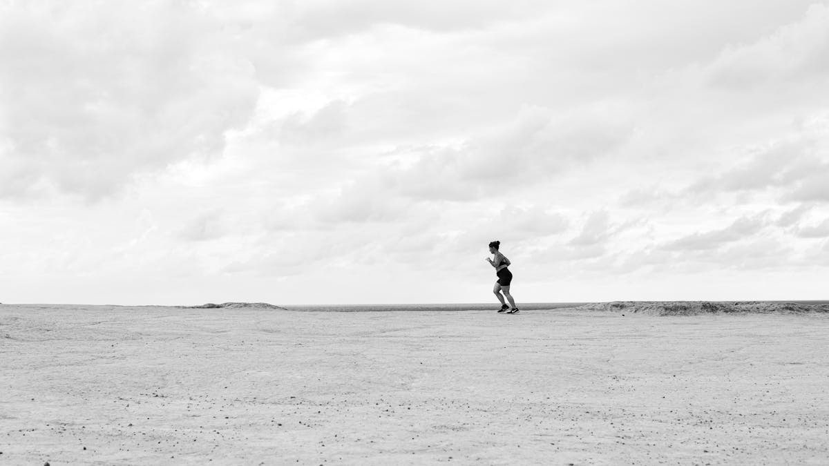 A lone runner on a vast, open terrain under a cloudy sky, captured in Natal, Brazil.
